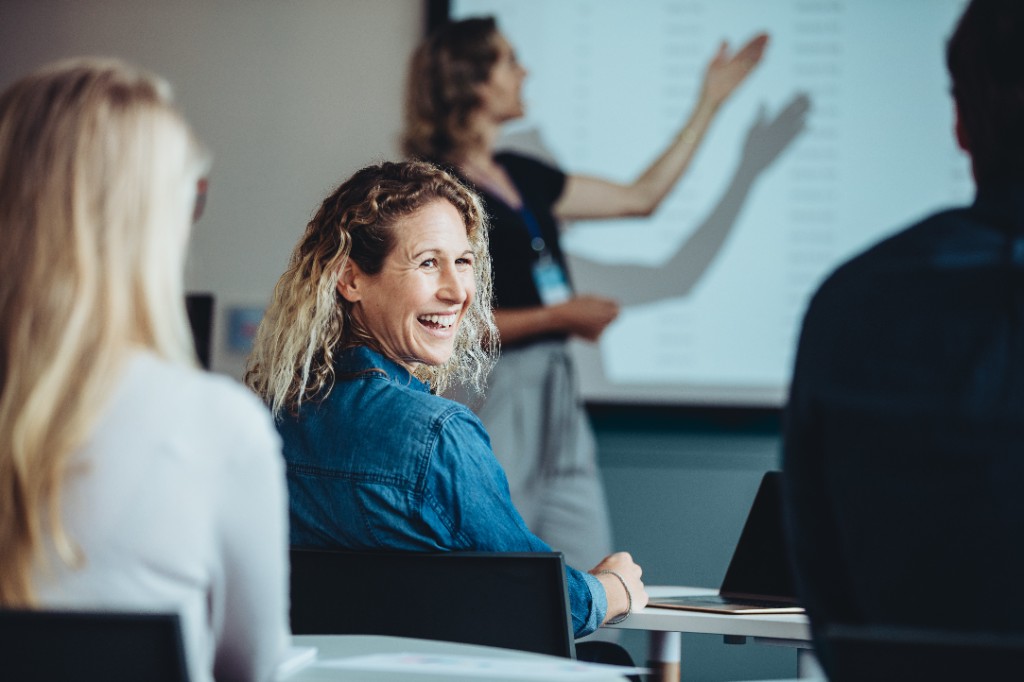 Participant laughing while a facilitator presents at the front — immersive over-the-shoulder framing.